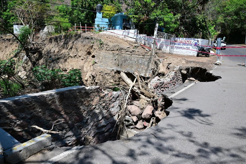Mal estado de una carretera debido a un deslizamiento de tierra, con un área colapsada y rodeada de vegetación.