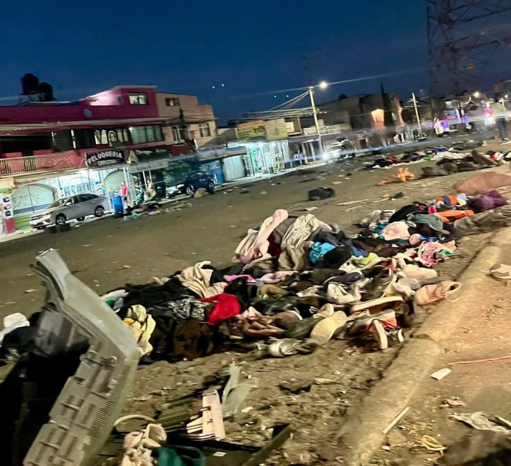 Camino desordenado con montones de ropa y objetos tirados, en un ambiente urbano y nocturno.