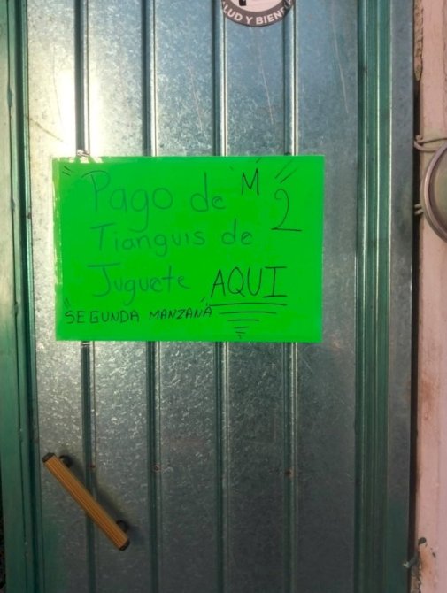 Cartel en una puerta que dice 'Pago de Tianguis de Juguete AQUÍ, SEGUNDA MANZANA'.