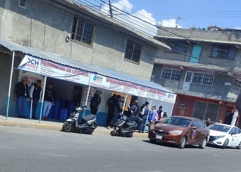 Tienda de productos de limpieza con varios clientes en la puerta, motocicletas estacionadas y vehículos pasando por la calle.