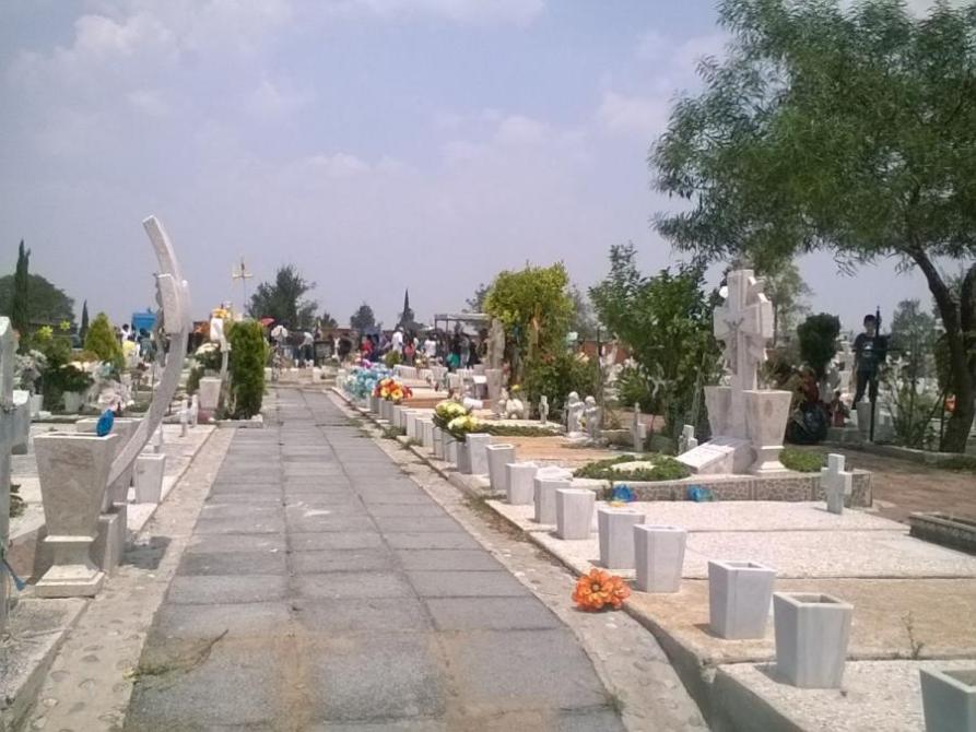 Cementerio con camino central, tumbas y flores decorativas, bajo un cielo nublado.