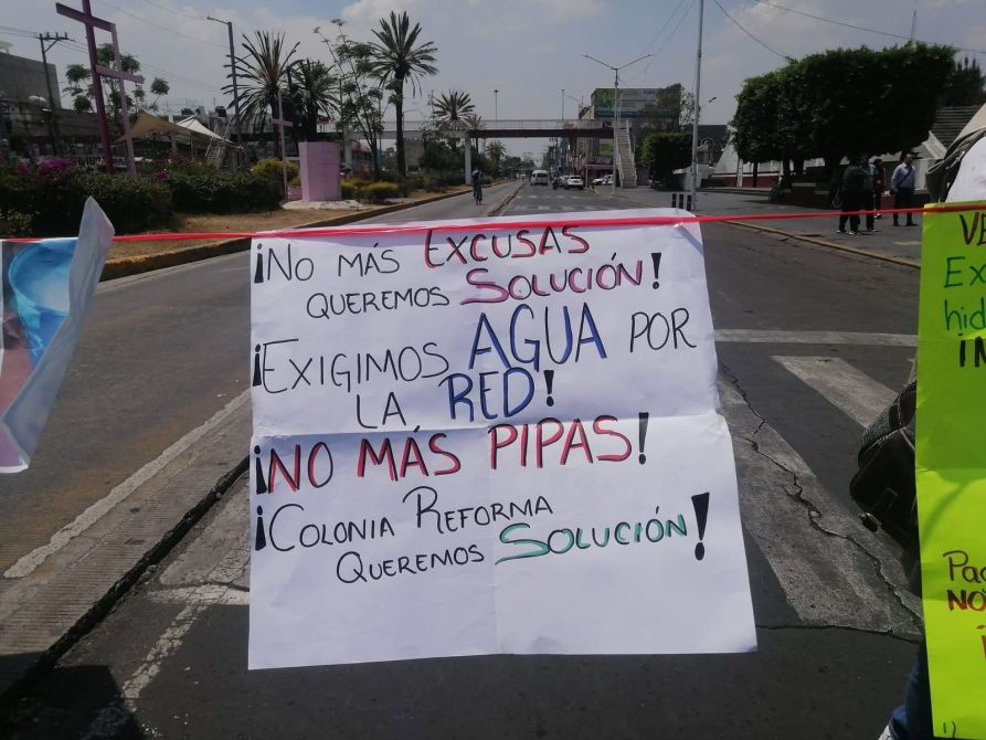 Carteles de protesta en la calle exigiendo soluciones para el suministro de agua, haciendo énfasis en la necesidad de agua por la red y rechazando el suministro en pipas.