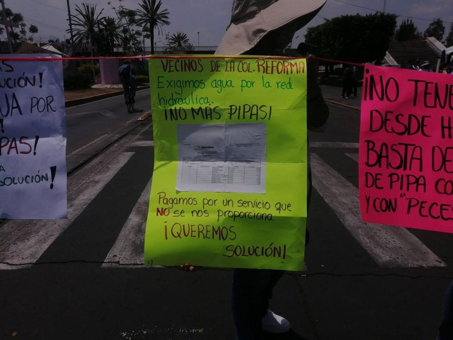 Carteles de protesta de vecinos exigiendo agua potable, con mensajes sobre el servicio que no se les proporciona y demandas de solución.