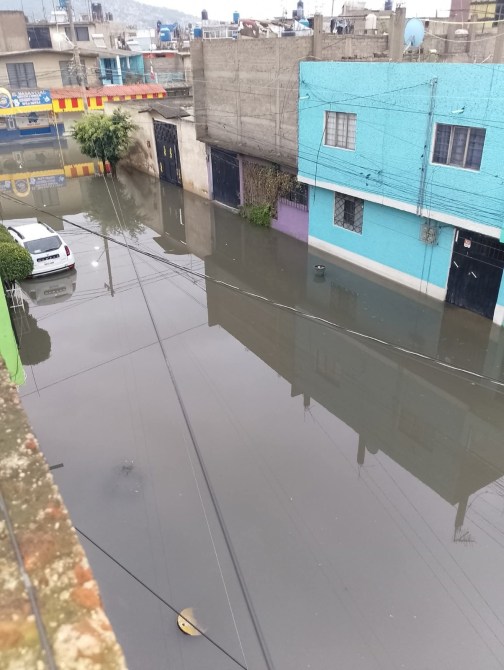 Inundación en una calle con edificios de colores y un automóvil parcialmente sumergido en agua.