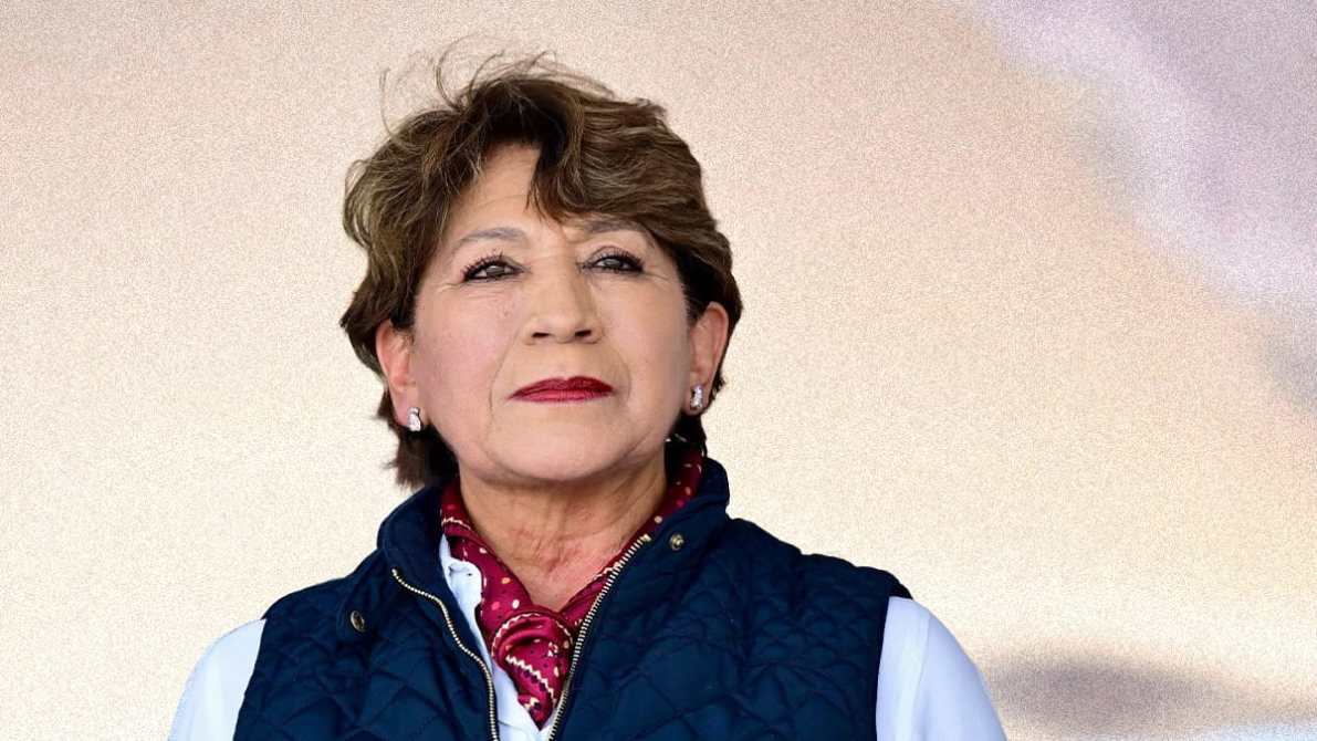 Retrato de una mujer de cabello corto y rizado, vistiendo un chaleco azul y una blusa blanca, con un pañuelo al cuello, mirando con confianza hacia la cámara.