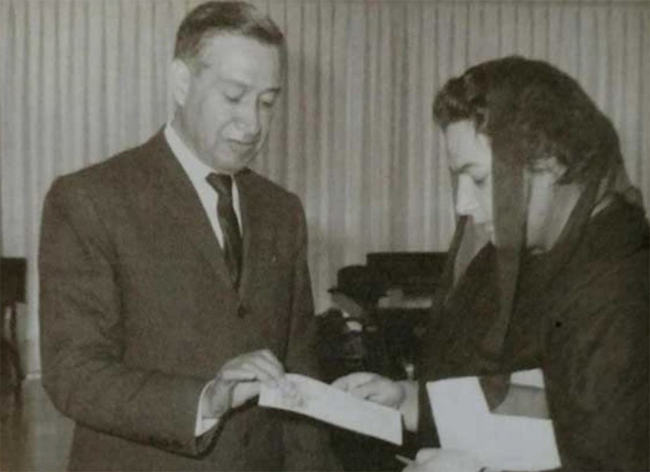 Un hombre y una mujer en una reunión, mirando un documento que sostiene el hombre mientras la mujer parece leerlo.