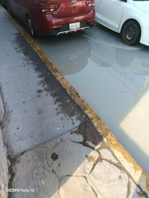 Una calle con dos autos estacionados, uno rojo y otro blanco, junto a una acera con un borde amarillo, en un día soleado.