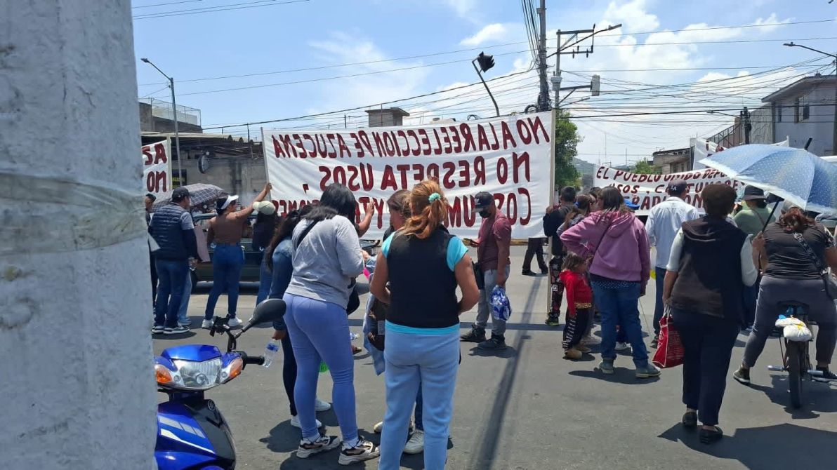Protesta en la calle con varias personas sosteniendo pancartas que expresan mensajes sobre derechos y rechazo a acciones específicas.