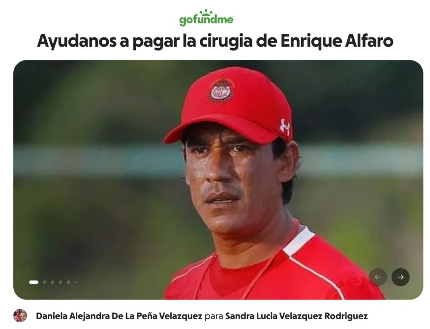Entrenador de fútbol luciendo una gorra roja y una camiseta roja, con fondo difuso.