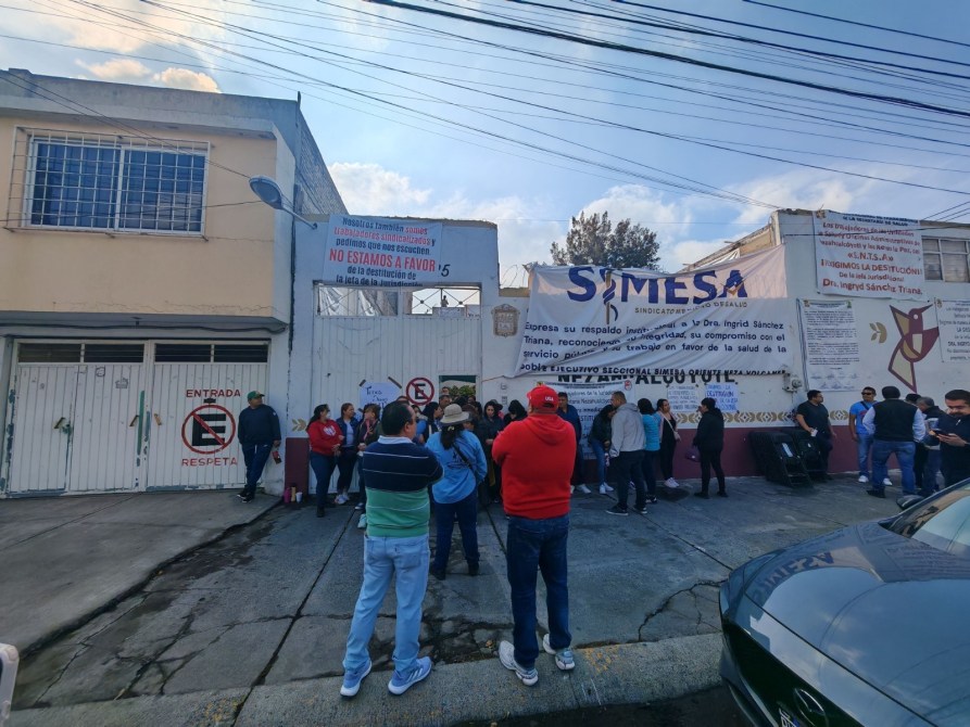 Grupo de personas frente a un edificio con pancartas de apoyo a la Dra. Ingrid Sánchez Tiana, en el contexto de un sindicato de salud.