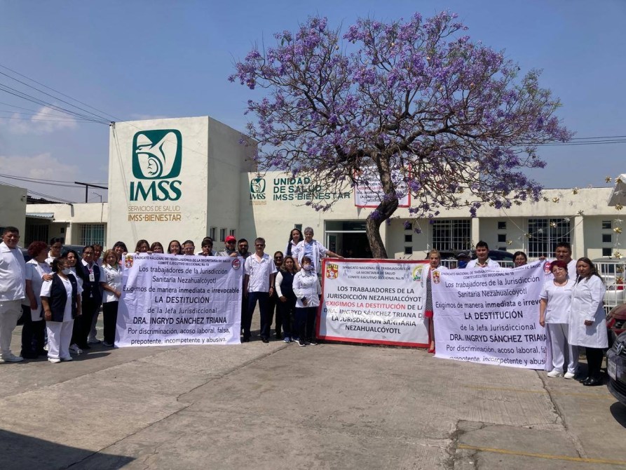 Grupo de trabajadores de la jurisdicción Sanitaria Nezahualcóyotl de IMSS, sosteniendo pancartas en protesta frente a su unidad de salud, exigiendo la destitución de la Dra. Ingrid Sánchez Triana.