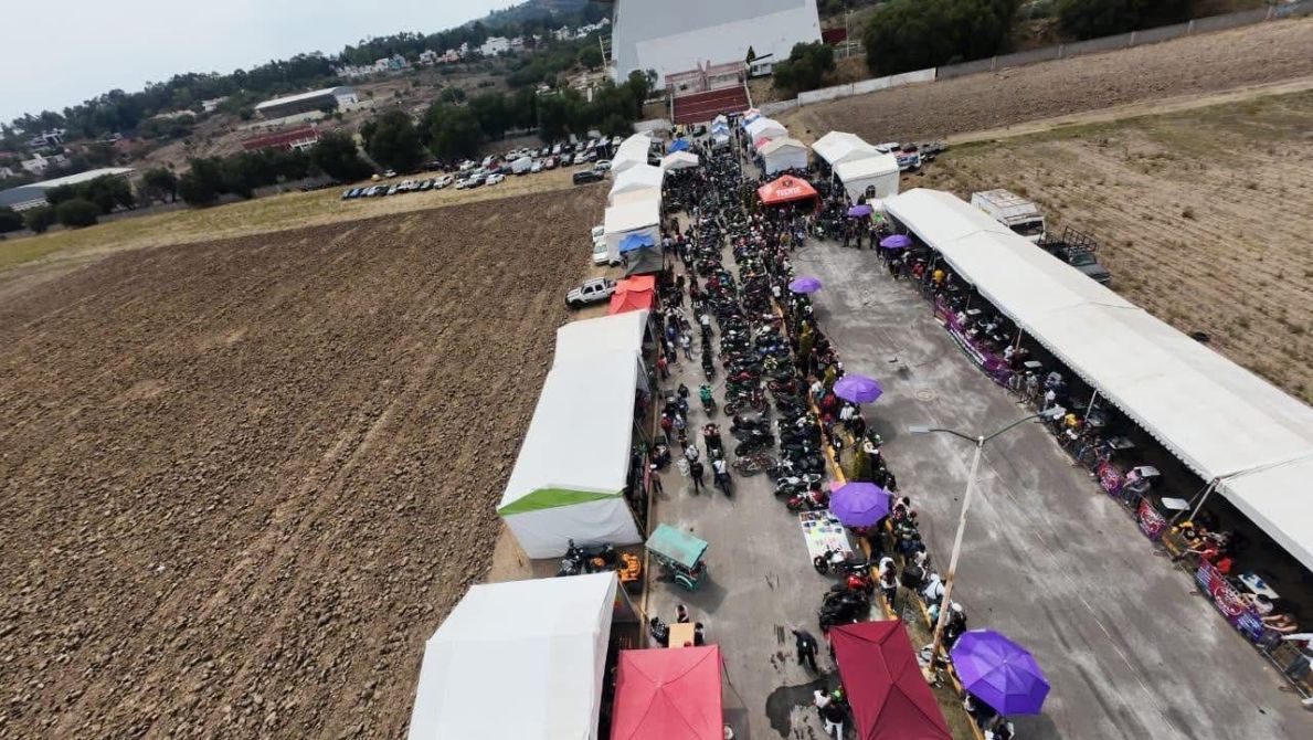 Vista aérea de un evento al aire libre con numerosos puestos y carpas. Se observa una multitud de personas y motocicletas estacionadas a lo largo de un camino.