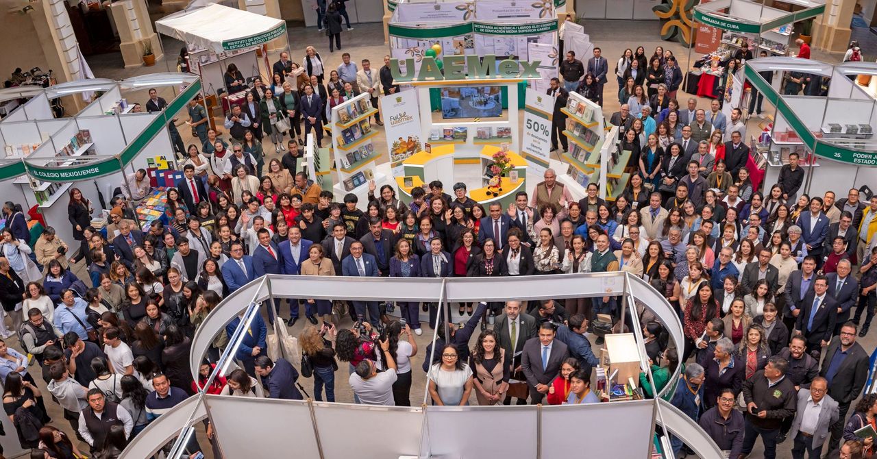 Multitud de personas posando en un evento, rodeados de estands de libros y material informativo, en un ambiente de celebración y encuentro cultural.