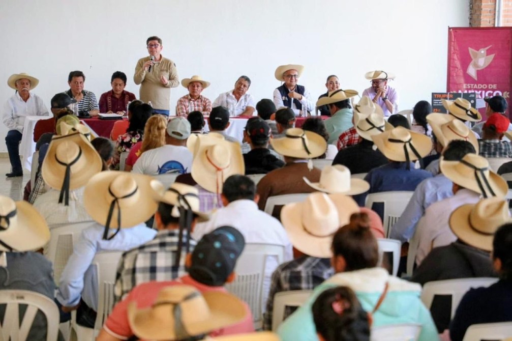 Reunión de agricultores con un orador en un evento, donde la mayoría de los asistentes llevan sombreros de paja, en un ambiente formal.