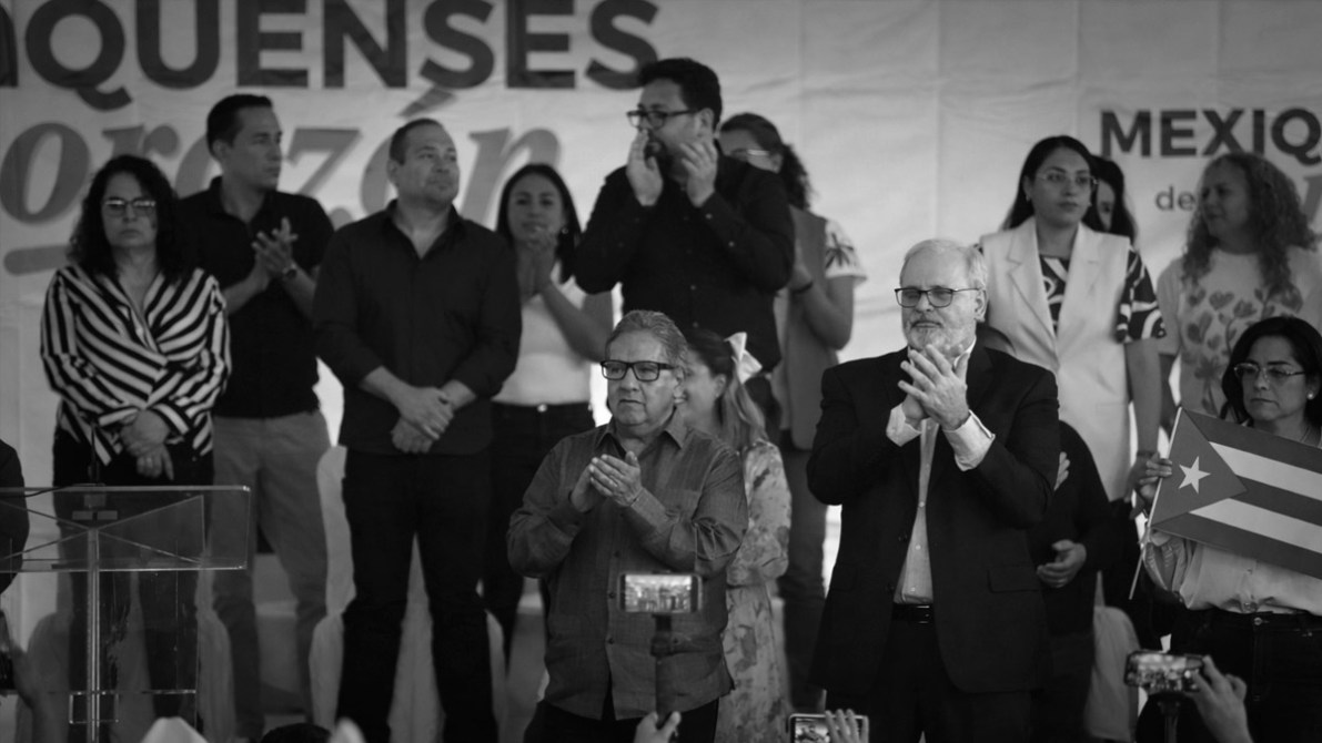 Grupo de personas aplaudiendo en un evento político, con un fondo que dice 'Mexicanos por una vida mejor'. En la imagen aparece una mujer sosteniendo una bandera cubana.