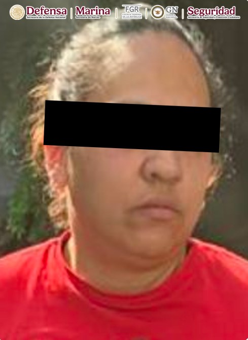 Mujer con camiseta roja y cabello recogido, mirando al frente con una expresión seria, fondo desenfocado.