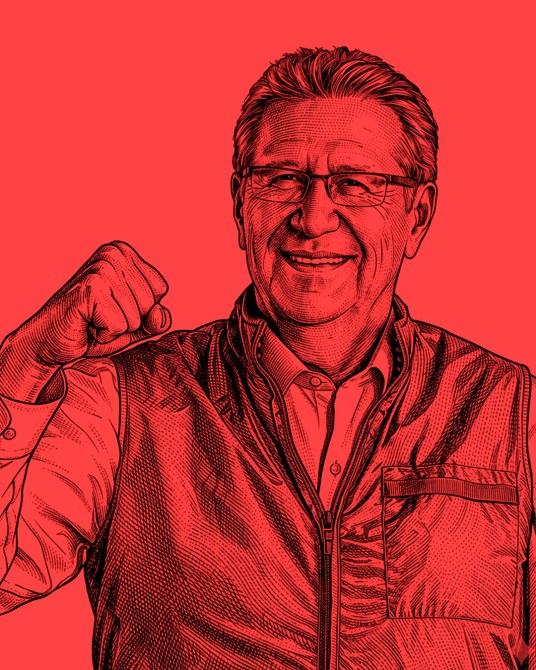 Retrato de un hombre sonriendo y levantando un puño en señal de triunfo, sobre un fondo rojo.