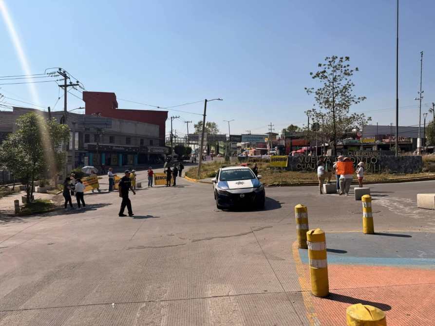 Vista de una calle con presencia de policías y un coche patrulla, además de señalización de seguridad y personas en la vía.