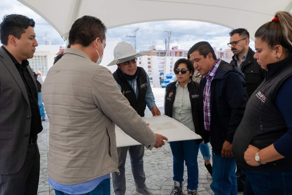 Grupo de personas discutiendo sobre un plano bajo una carpa, en un ambiente urbano.