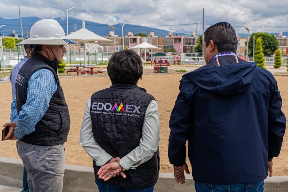 Tres personas observando un área recreativa al aire libre, con un hombre usando un casco blanco y otros dos vistiendo chalecos con el logo de EDOMEX.