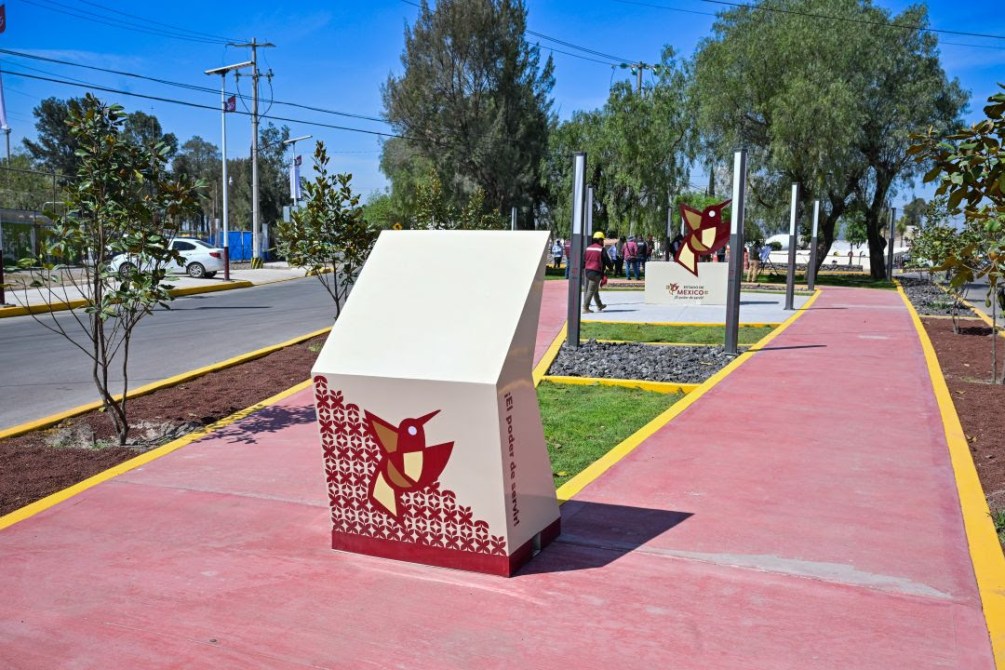 Espacio urbano con esculturas y carteles decorativos en un camino pavimentado, rodeado de áreas verdes y árboles.