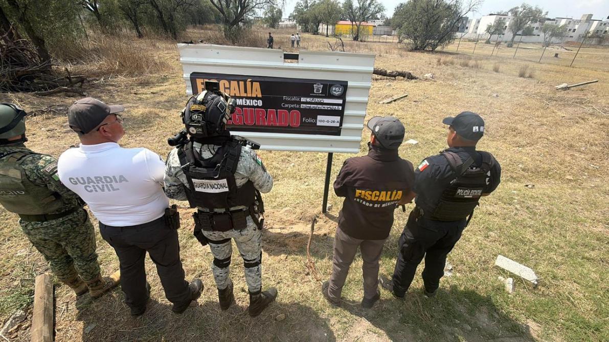 Integrantes de las fuerzas de seguridad observando un letrero de la Fiscalía en un terreno baldío en México.