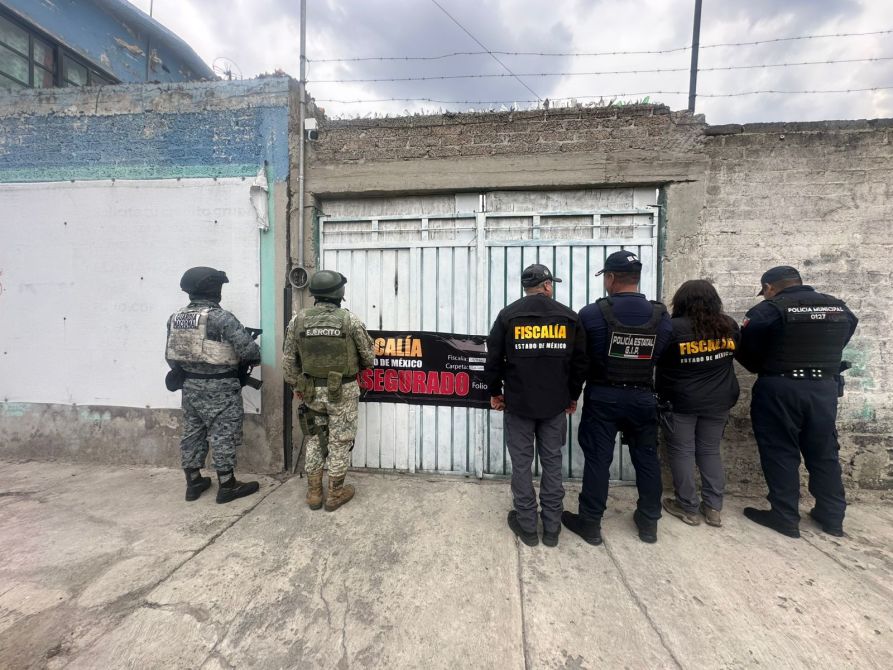 Un grupo de agentes de seguridad y fiscales se encuentra frente a una puerta cerrada con un cartel que dice 'ASEGURADO'.