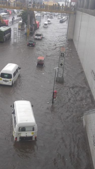 Inundación en una calle urbana con vehículos sumergidos parcialmente en agua.