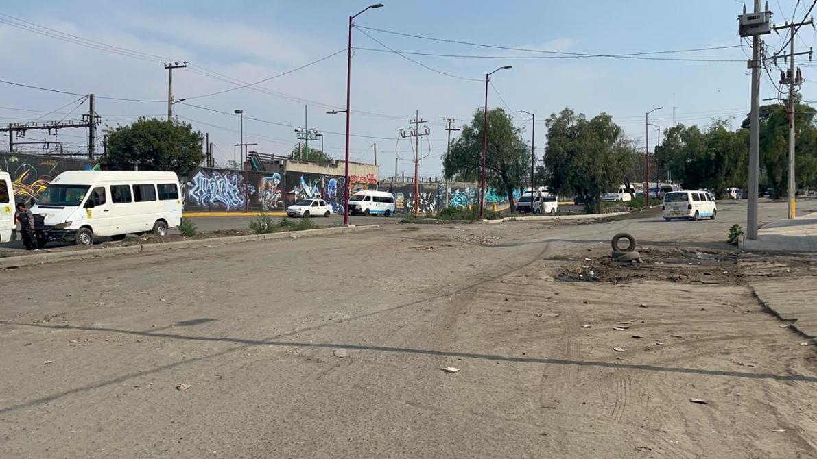 Una calle polvorienta con varias vans blancas y un automóvil, rodeada de grafitis coloridos en una pared cercana.