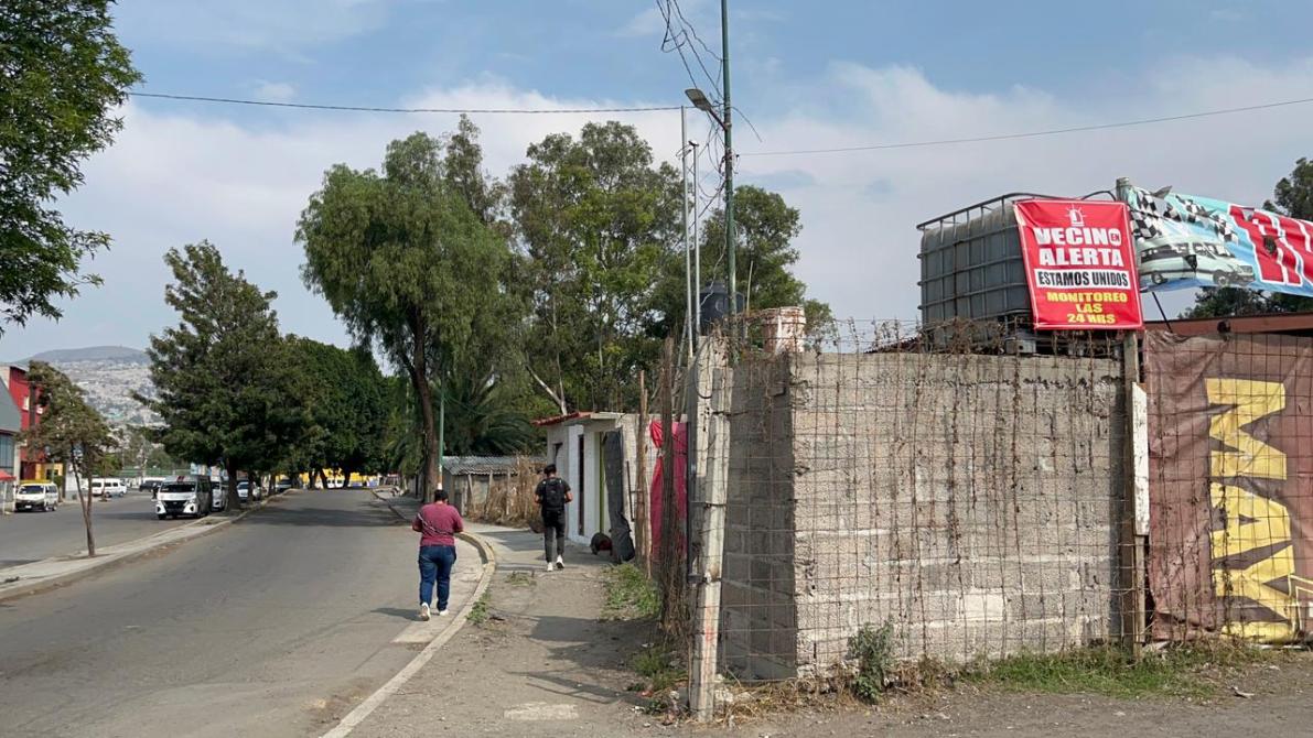Vista de una calle con árboles, casas y un letrero de advertencia sobre vigilancia vecinal.