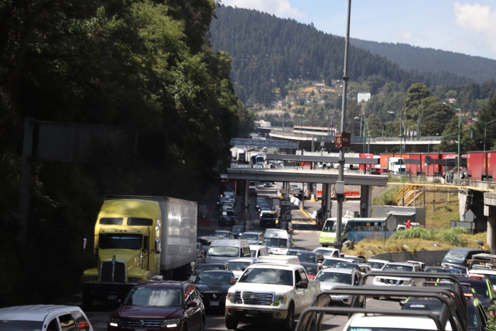Tráfico denso en una carretera con vehículos de diferentes tamaños, incluyendo un camión amarillo, en un paisaje montañoso.