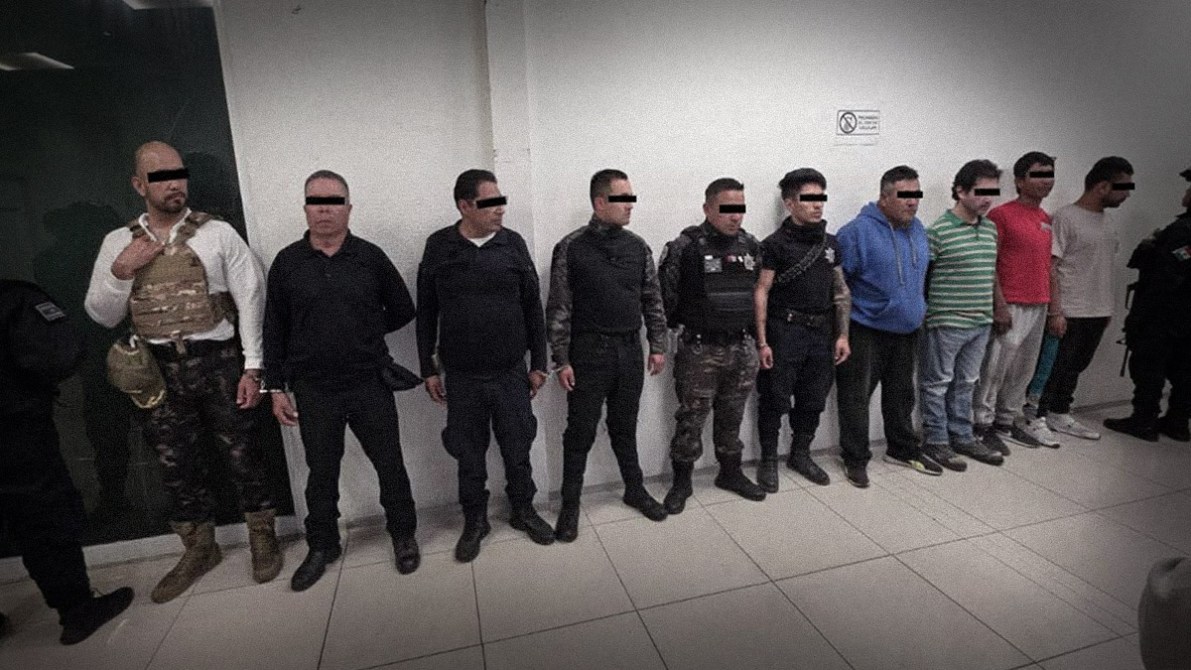 Ocho hombres alineados en una sala, algunos vestidos de civil y otros con uniformes de seguridad, con la mayoría de sus rostros cubiertos.