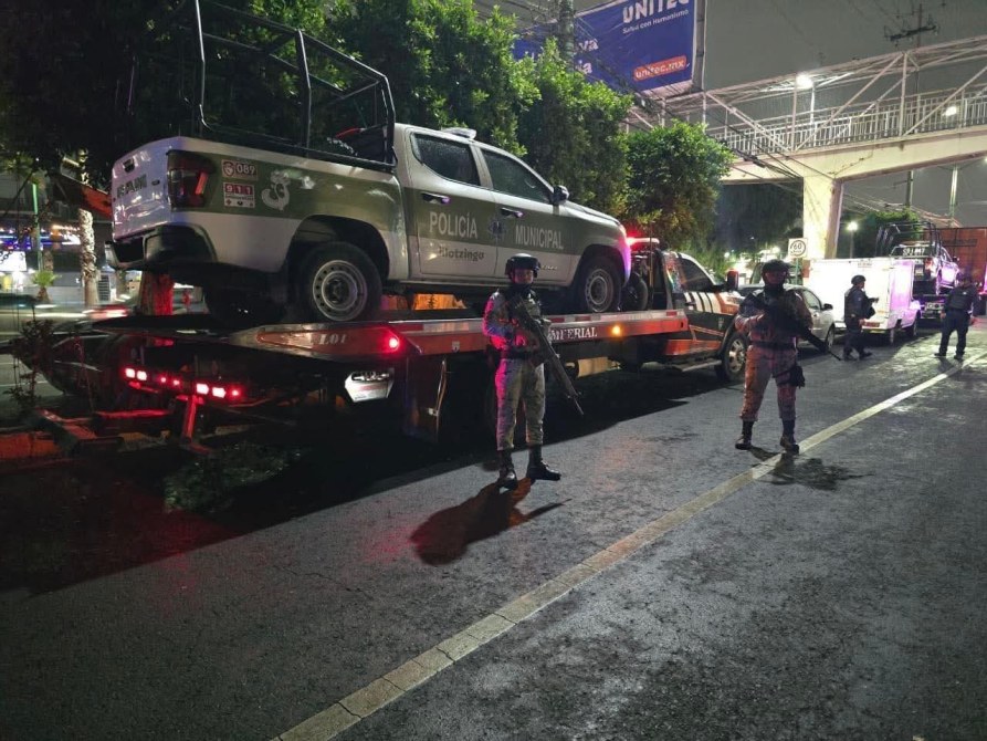 Policía municipal montada en una grúa durante la noche, con vehículos y oficiales armados en el lugar.
