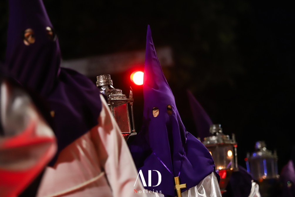 Participantes de una procesión con capirotes morados sosteniendo faroles en un ambiente nocturno.