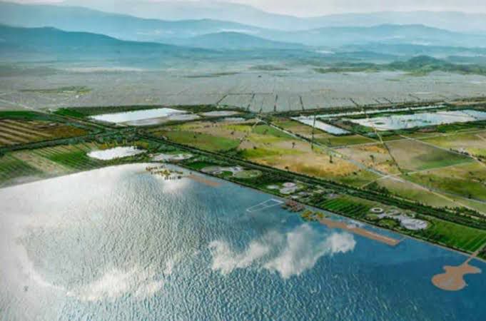 Vista aérea de un paisaje que incluye agua, campos agrícolas y montañas al fondo.