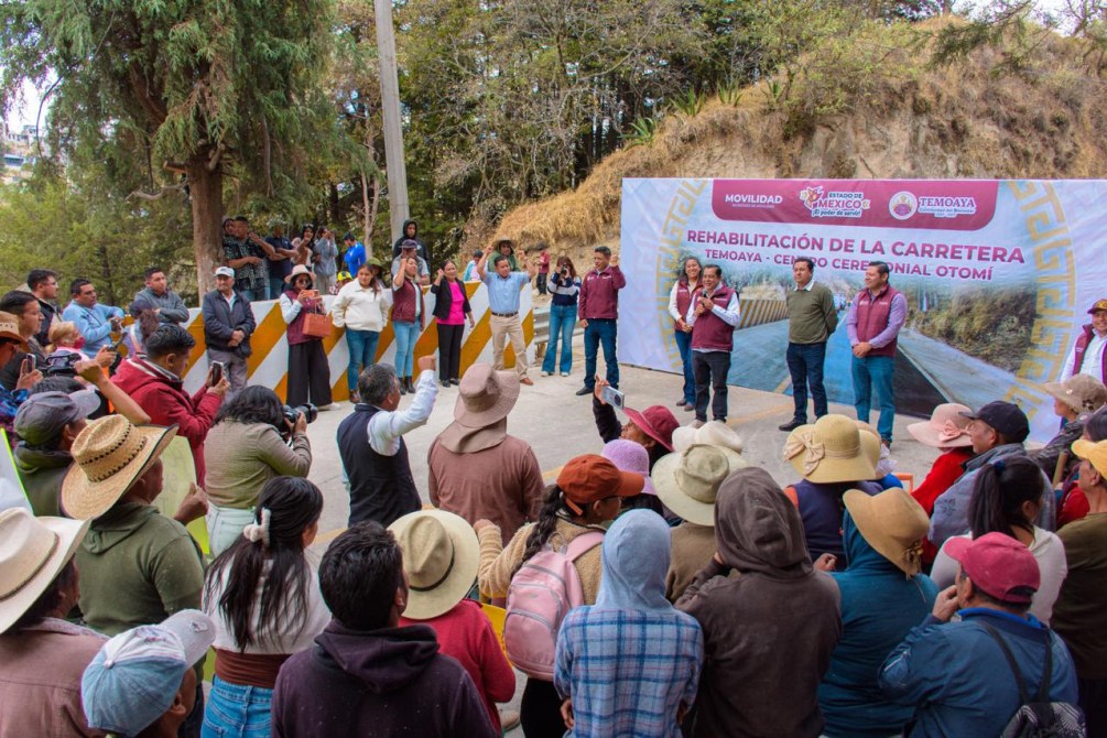 Evento comunitario sobre la rehabilitación de la carretera en Temoaya, con asistentes escuchando a los oradores y un banner informativo al fondo.