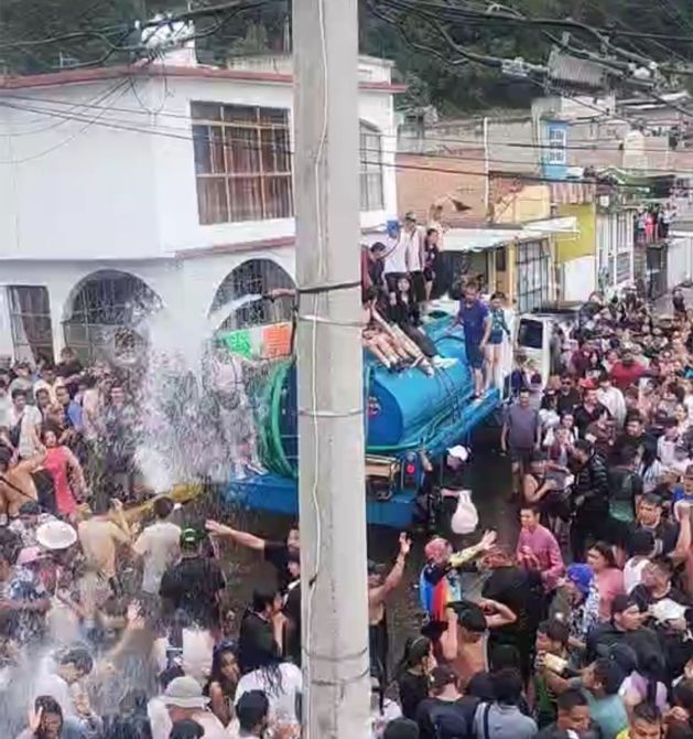 Multitud de personas celebrando en la calle con un camión de agua, mientras se celebra un festival.