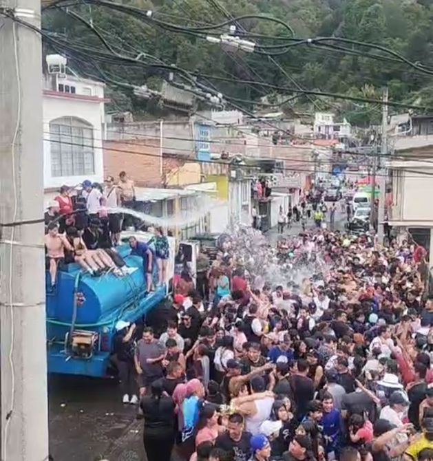 Multitud de personas en una calle, celebrando y divertiéndose, con un camión de agua que rocía agua sobre la gente.