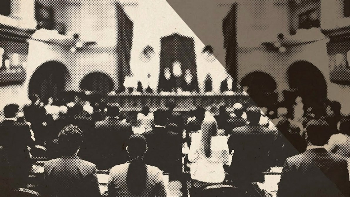 Vista de un salón de sesiones con representantes en asamblea, enfocándose en la parte posterior de los asistentes.