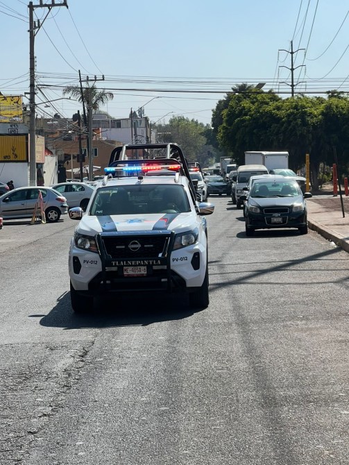 Vehículo policial con luces intermitentes en una calle de la ciudad, rodeado de tráfico.