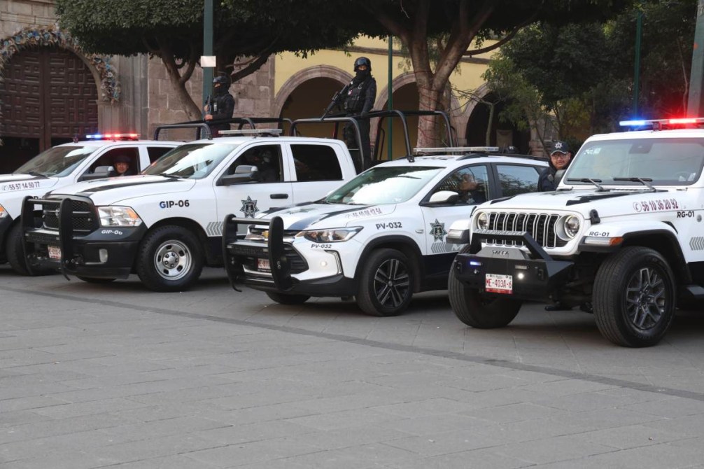 Varios vehículos de policía en una calle, con luces de emergencia activadas y oficiales a bordo.