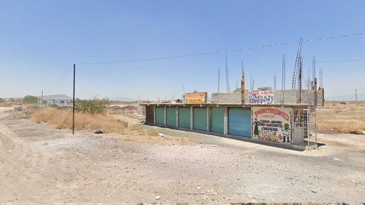 Vista de una tienda con persianas cerradas en un área rural, rodeada de terreno seco y escombros.