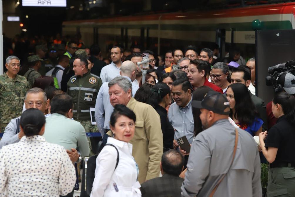 Multitud de personas en un evento público, incluyendo miembros de seguridad y funcionarios, en un espacio cerrado.