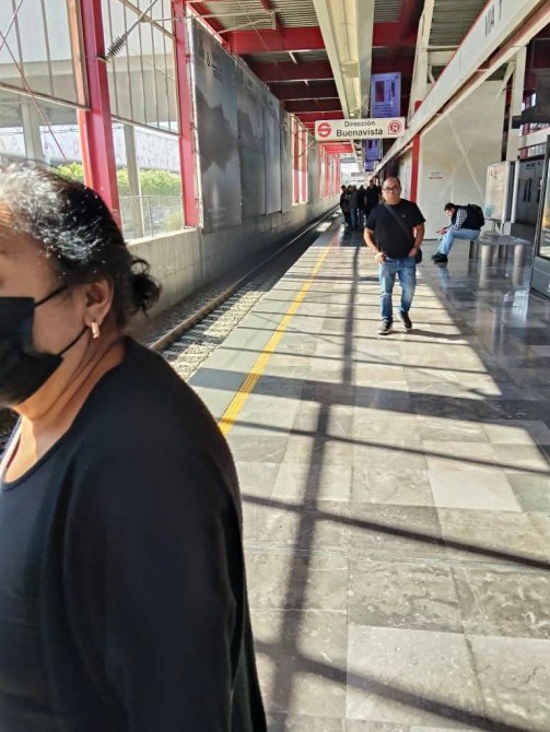 Estación de transporte público con pasajeros en la plataforma, algunos usando mascarillas.