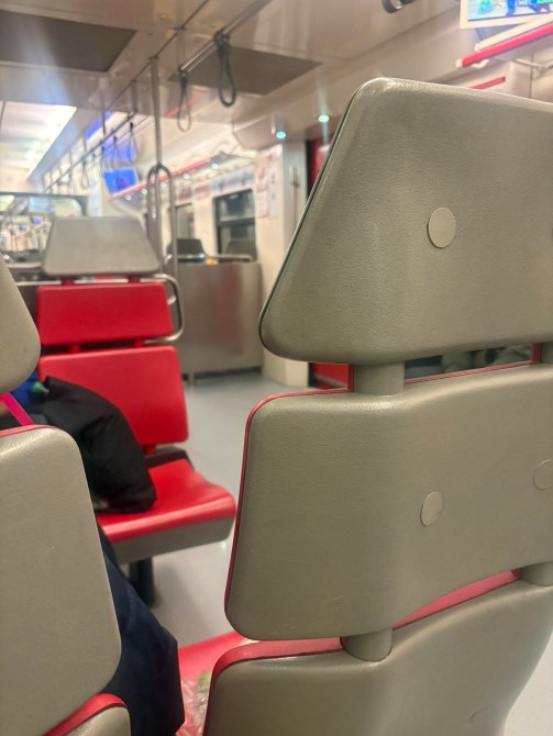 Asiento de tren con respaldo gris y un fondo de asientos rojos en un vagón de metro vacío.