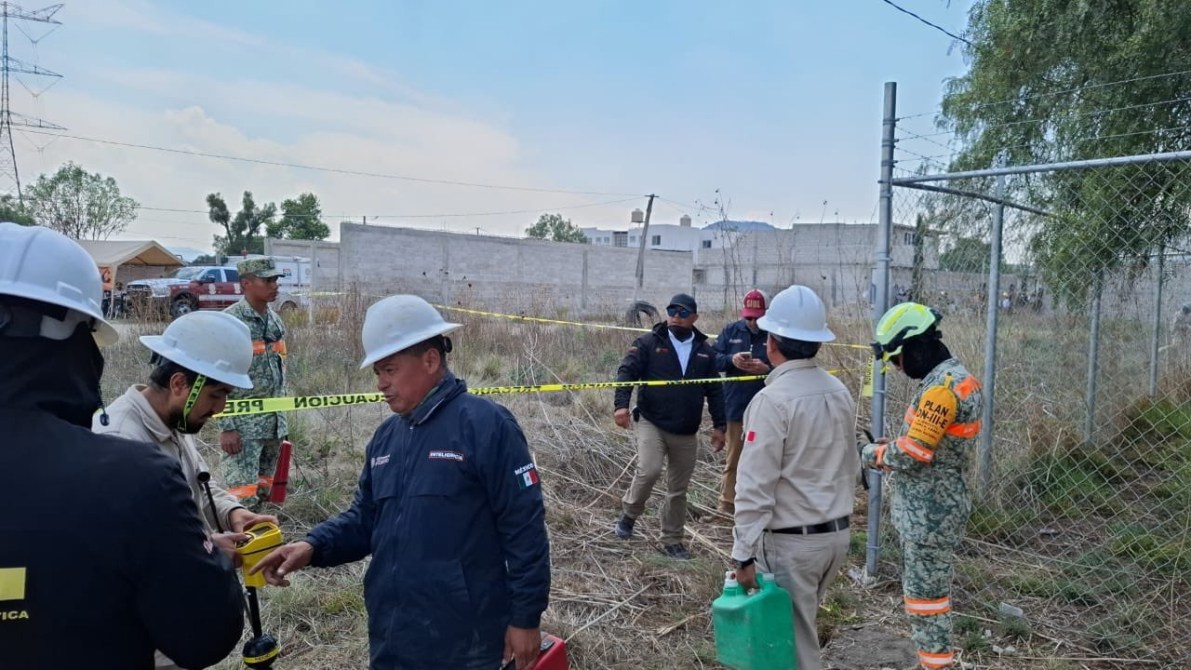 Grupo de personas con cascos de seguridad en un área cercada con cinta de advertencia, trabajando en un sitio al aire libre.