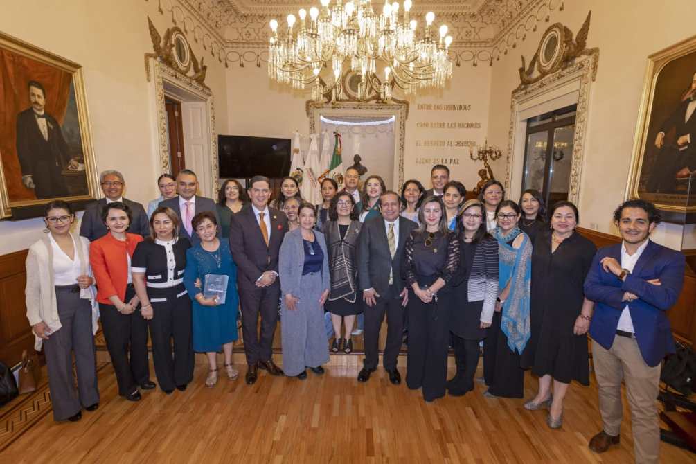 Grupo de personas posando en un salón con decoración elegante, incluido un candelabro y retratos en las paredes.