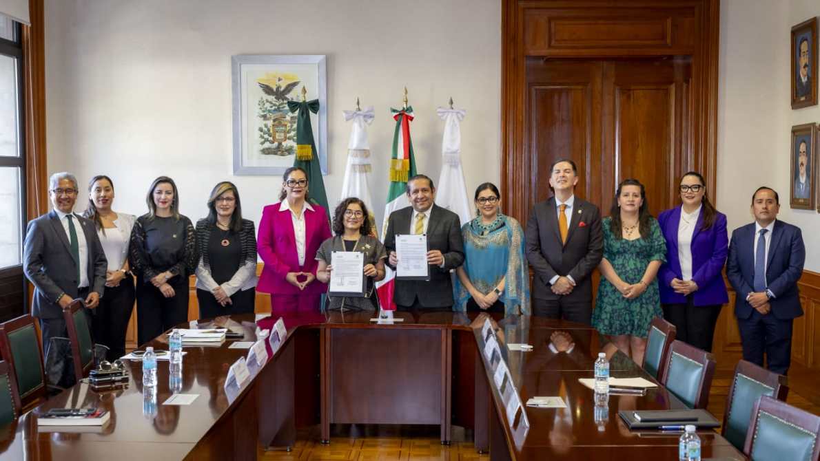 Reunión formal en una sala con representantes sosteniendo documentos firmados, rodeados de banderas y cuadros en la pared.