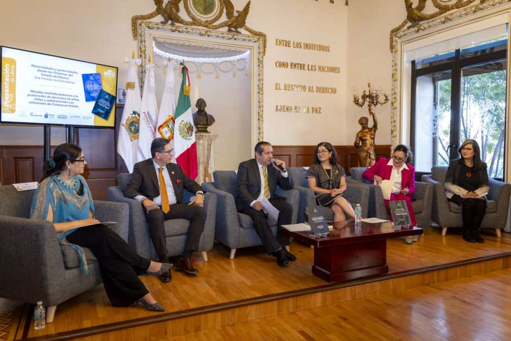 Presentación de un evento con varios panelistas sentados en un salón, con banderas nacionales y una pantalla de proyección al fondo que muestra un tema relacionado con derechos humanos.