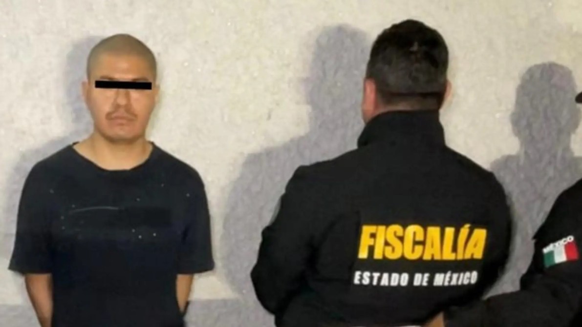 Hombre detenido frente a un muro, con un agente de la fiscalía de espaldas, en un entorno de investigación criminal.